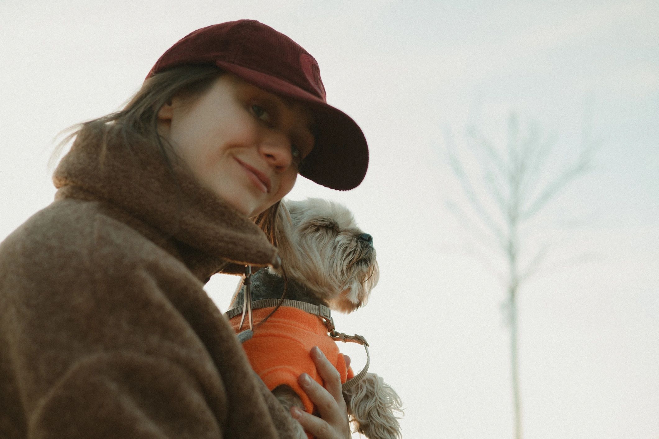 Woman holding a small dog wearing an orange sweater outdoors